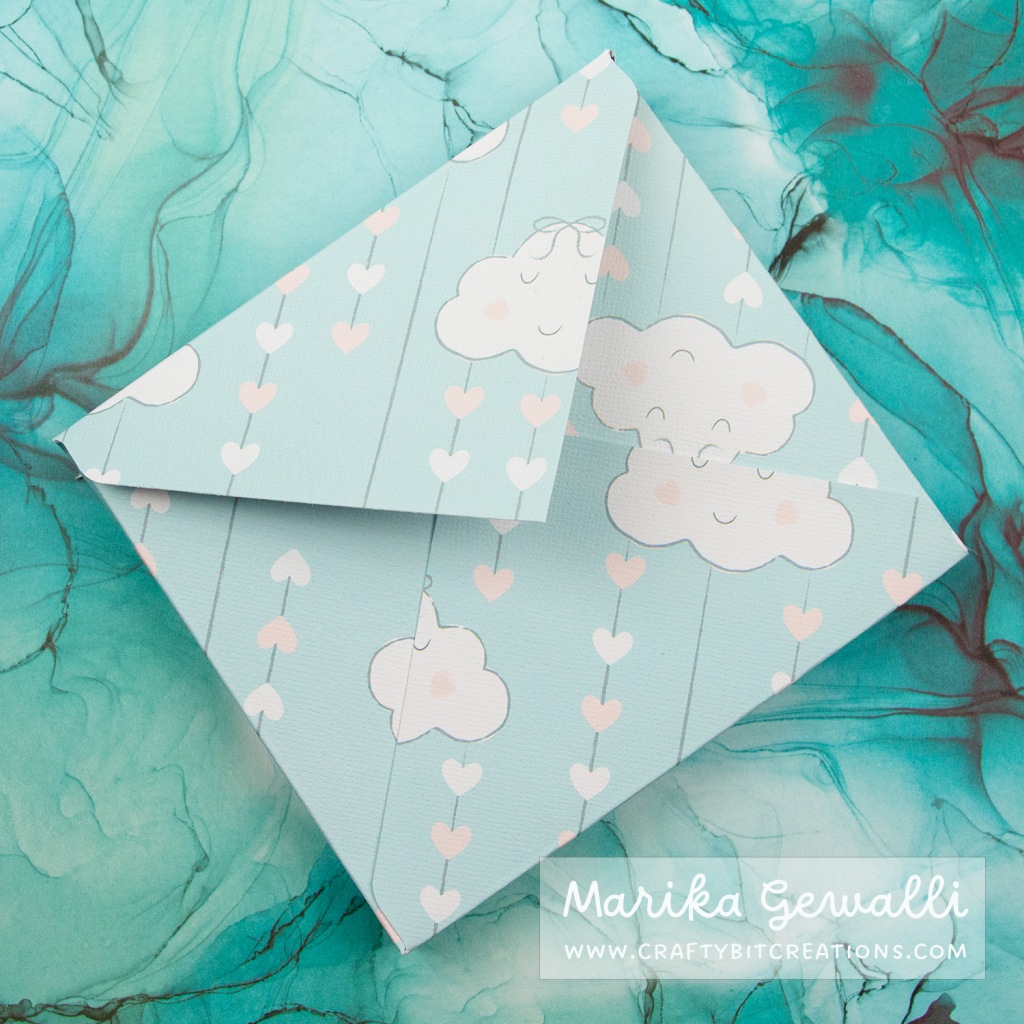 Closeup of a box envelope made from pattern paper with clouds and strings of heart on.